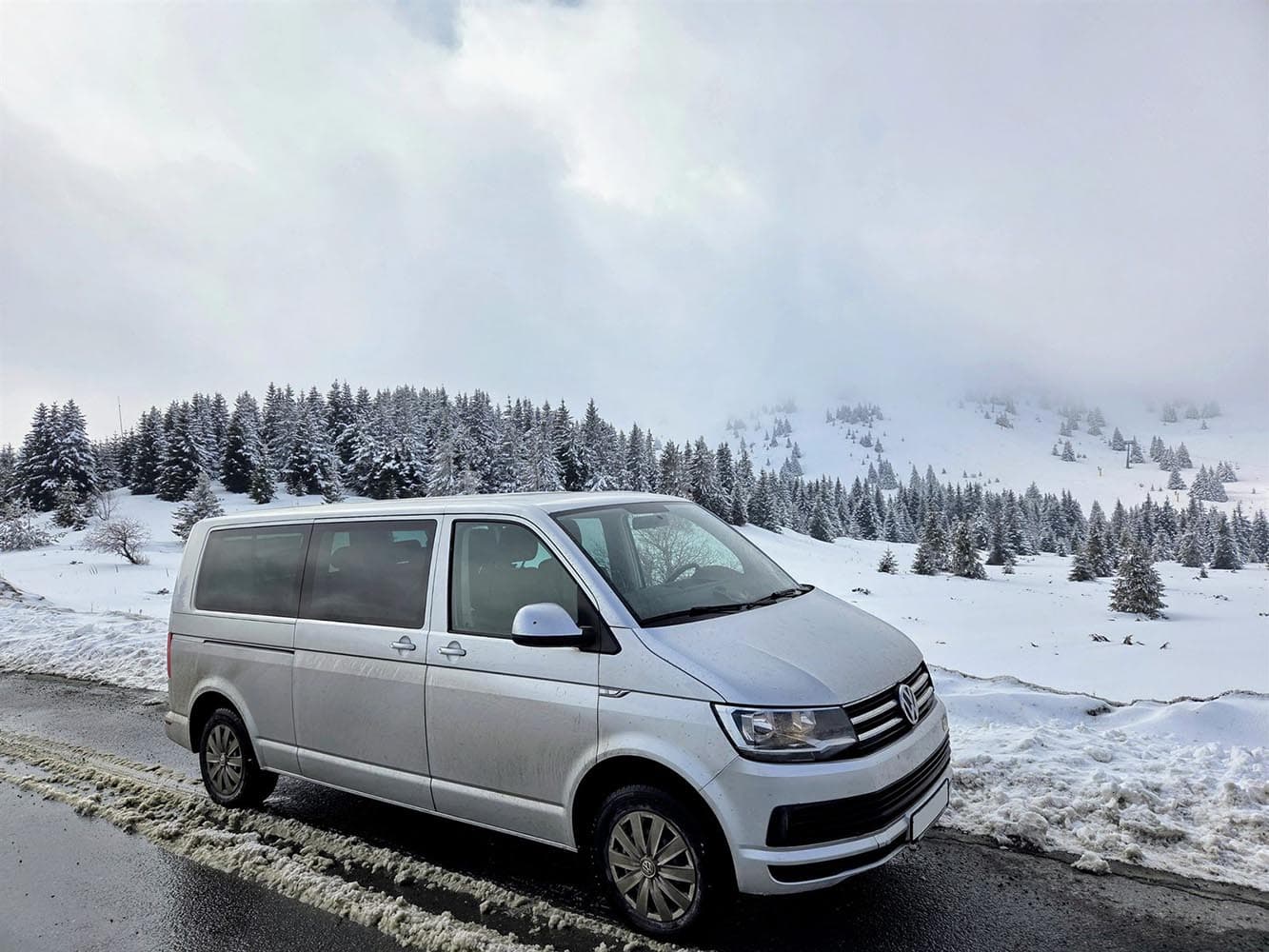 Beli Volkswagen kombi na zimskom putu sa planinskim pejzažom